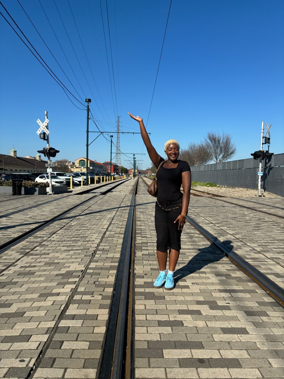 Nzinga balancing on train tracks with arms outstretched under a clear blue sky