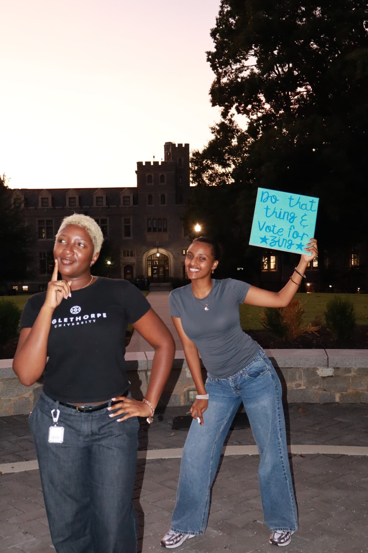 Nzinga and a friend posing at dusk on campus, holding the painted Vote for Zing sign