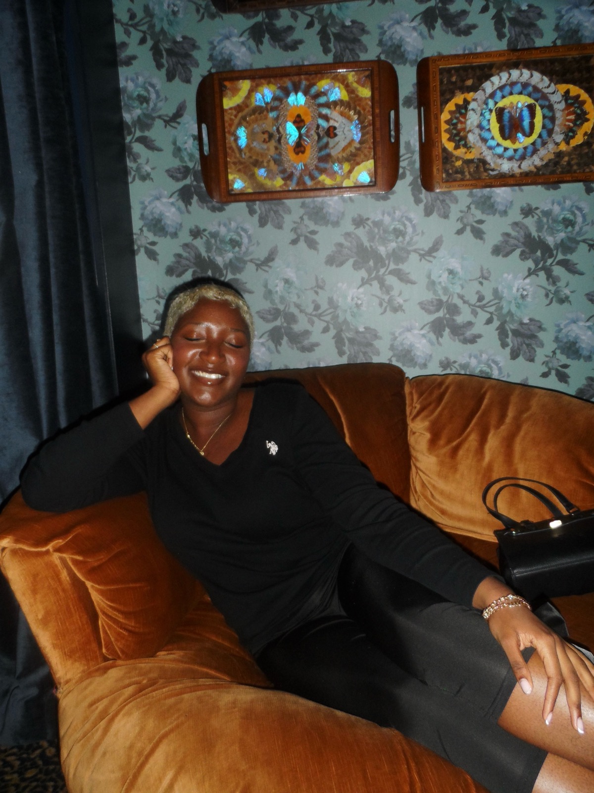 Nzinga laughing with eyes closed on a velvet sofa