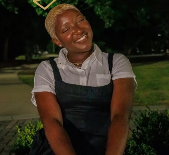 Nzinga smiling outdoors in a white shirt and dark dress