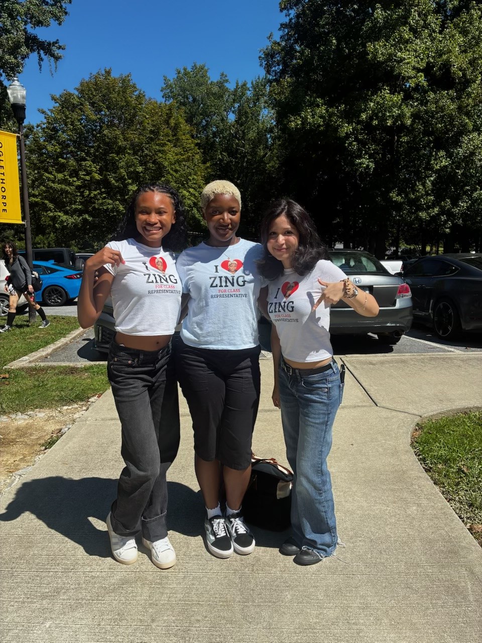 Nzinga and two friends wearing matching I heart Zing campaign shirts on a sunny sidewalk