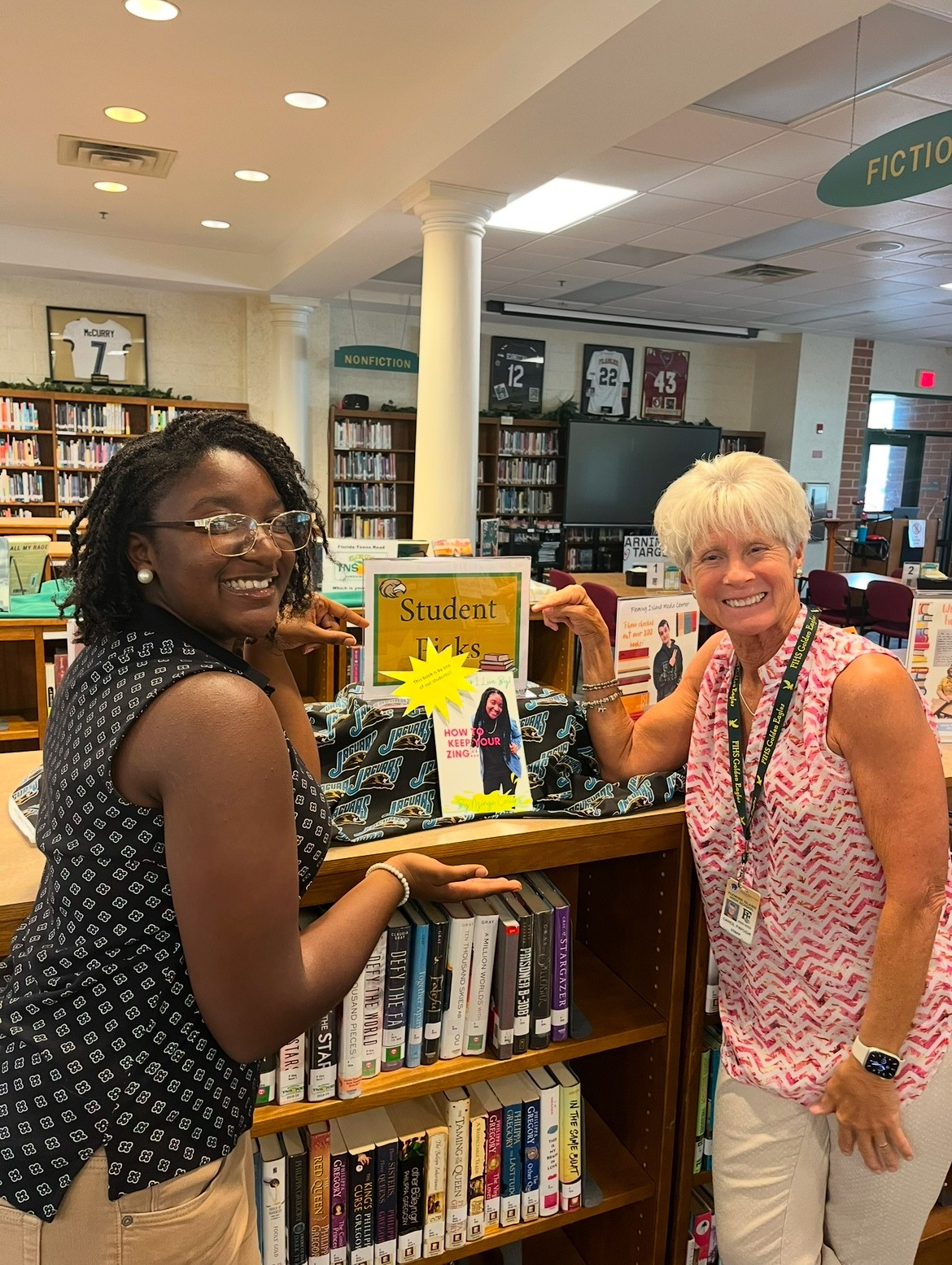 Nzinga and a woman smiling beside a display of her book in a library